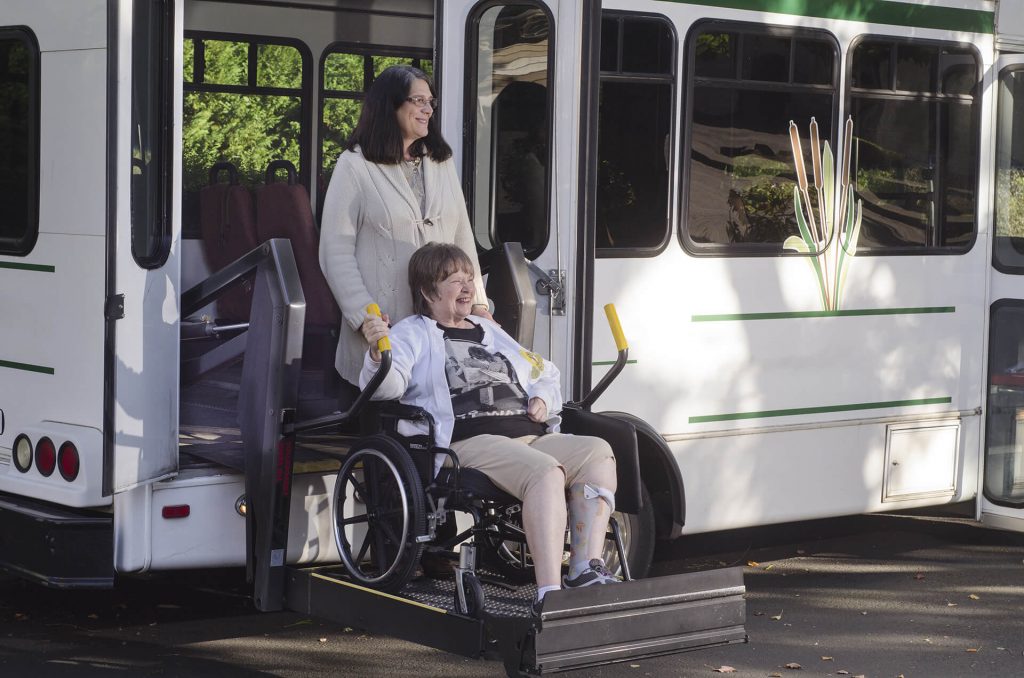 Woman in wheelchair being assisted off the bus with mobility device.