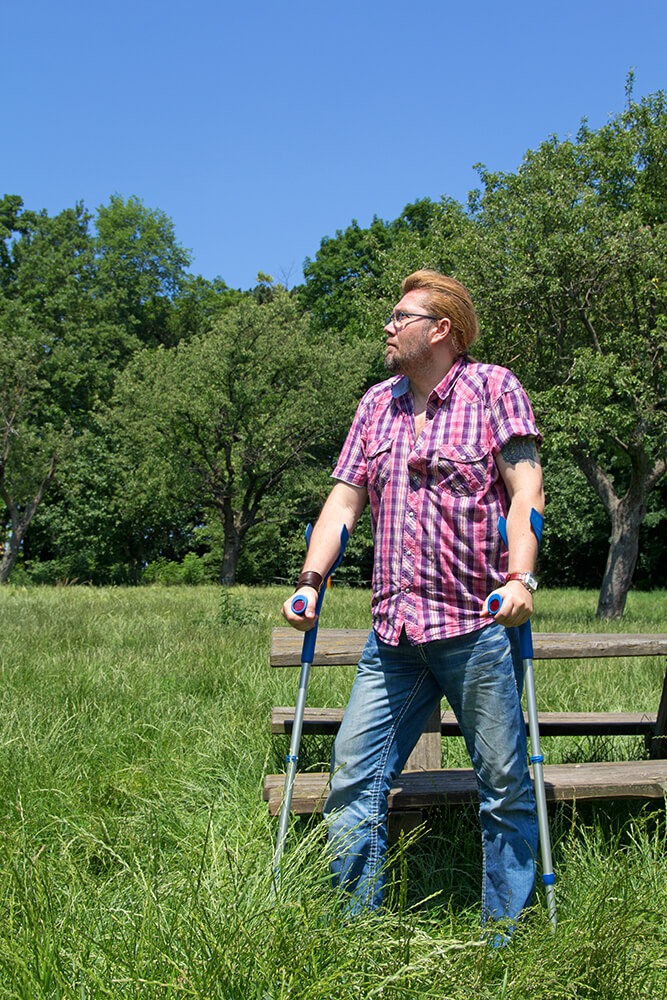 Man at picnic bench in field using crutches.